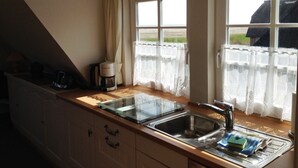 A kitchen with a sink, a coffee maker, and a window with curtains. - Watt'n Blick, 70sqm for up to 4 people - Haus am Wattenmeer (Sylt)