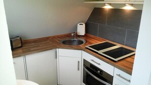A compact kitchen with a sink, two stovetops, a toaster, and a built-in oven. - Wadden runner, 40sqm for up to 2 people - Haus am Wattenmeer (Sylt)