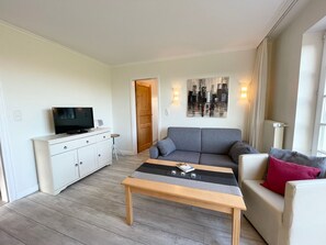 Een moderne woonkamer met een grijze bank, een houten salontafel, een witte tv-meubel en een schilderij aan de muur.