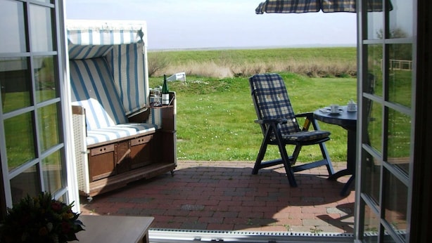 A patio with a striped chair, a plaid chair, and a table with an umbrella. - Watt'n Idyll, 50sqm for up to 2 people - Haus am Wattenmeer (Sylt)