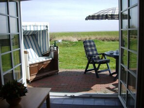 A patio with a striped chair, a plaid chair, and a table with an umbrella. - An idyllic spot on the mudflat, 50 m² for up to 2 people—A house on the Wadden Sea (Sylt)