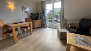 A modern living room with a dining area, a flat-screen TV, and a large sliding glass door leading to an outdoor balcony.