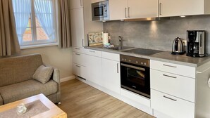 A compact kitchen with white cabinets, a built-in microwave, a stove, and a coffee maker.