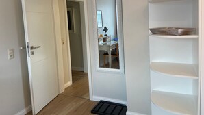 A hallway with a white door, a mirror, and a white shelving unit.