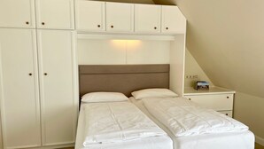A bedroom with two single beds, a large wardrobe, and a nightstand with a lamp. - Starfish, 30sqm for up to 2 people - Haus an den Wiesen (Sylt-Ost)