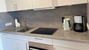 A kitchen with white cabinets, a stainless steel sink, a built-in stovetop, and a coffee maker. - Starfish, 30sqm for up to 2 people - Haus an den Wiesen (Sylt-Ost)