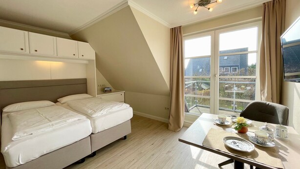 A bedroom with a bed, a desk, and a window with curtains. - Starfish, 30sqm for up to 2 people - Haus an den Wiesen (Sylt-Ost)