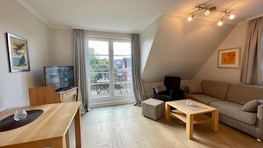 En moderne stue med spiseplads, sofa, fjernsyn og en balkon med bord og stole.