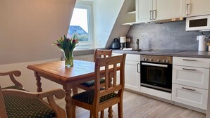 Une cuisine moderne avec des armoires blanches, un four encastré et un coin repas comprenant une table et des chaises en bois.