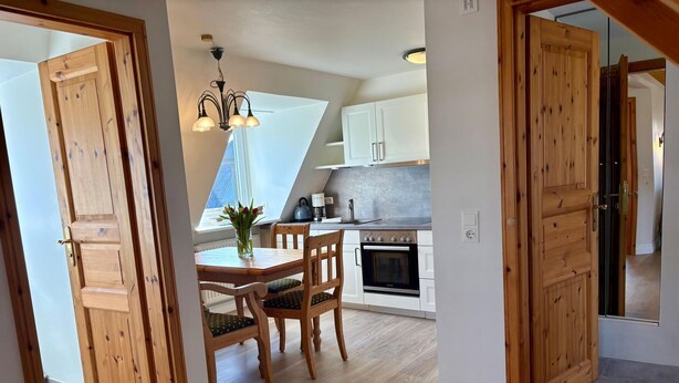 Un coin repas avec une table et des chaises en bois, un lustre et une vue sur la cuisine.