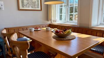 A dining area with a wooden table, bench seating, a bowl of fruit, and a framed map on the wall.