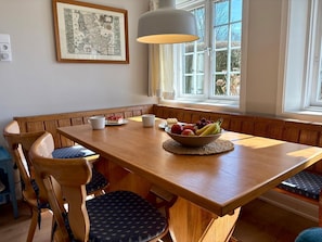 Un comedor con una mesa de madera, asientos tipo banco, un cuenco de fruta y un mapa enmarcado en la pared.