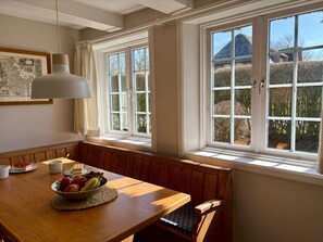 A dining area with a wooden table, white chairs, a bowl of fruit, and a framed map on the wall. - Appartement West, 45qm für bis zu 2 Personen - Altes Friesenhaus (Sylt-Ost)