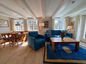 A living room with a sofa, coffee table, and dining area with chairs and a table. - Appartement West, 45qm für bis zu 2 Personen - Altes Friesenhaus (Sylt-Ost)