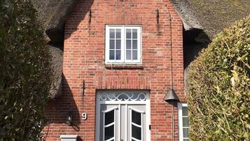 A red brick house with a thatched roof, a white double door, and a small window above the door.