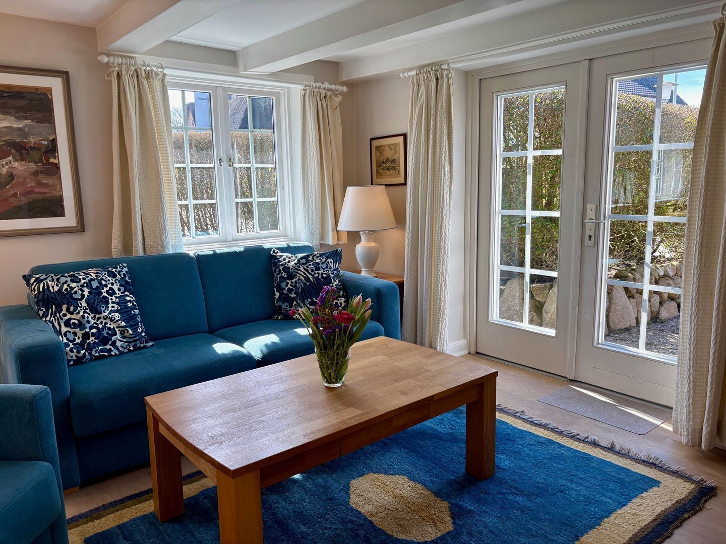 A living room with a blue sofa, a wooden coffee table, and a view through large glass doors.