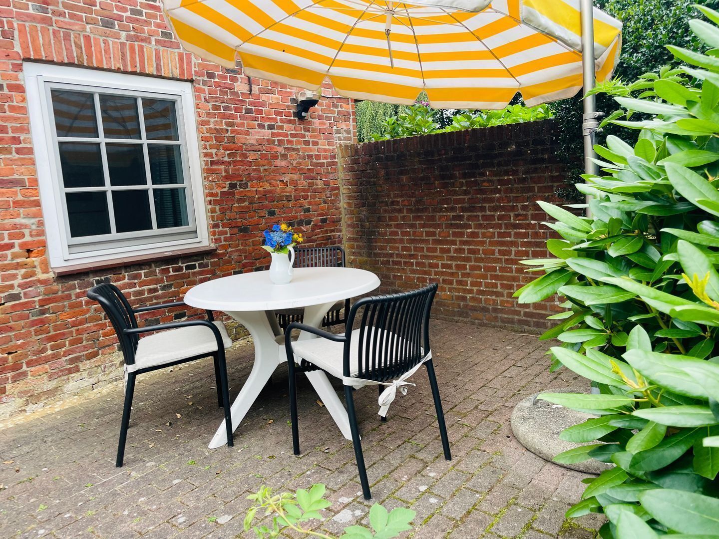 A patio with a white table and black chairs, a yellow and white striped umbrella, and a brick wall.