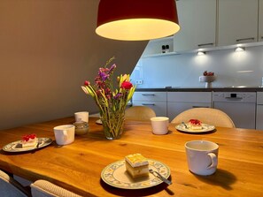 A dining table with a vase of flowers, two plates with cake, and two white cups. - Unterm Reet, 100qm für bis zu 5 Personen - Altes Friesenhaus (Sylt-Ost)
