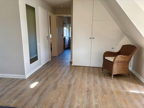 A room with wooden flooring, a wicker chair, and a white wardrobe. - Unterm Reet, 100qm für bis zu 5 Personen - Altes Friesenhaus (Sylt-Ost)