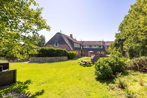 A house with a thatched roof, a stone wall, and a grassy yard with a picnic table. - Unterm Reet, 100qm für bis zu 5 Personen - Altes Friesenhaus (Sylt-Ost)