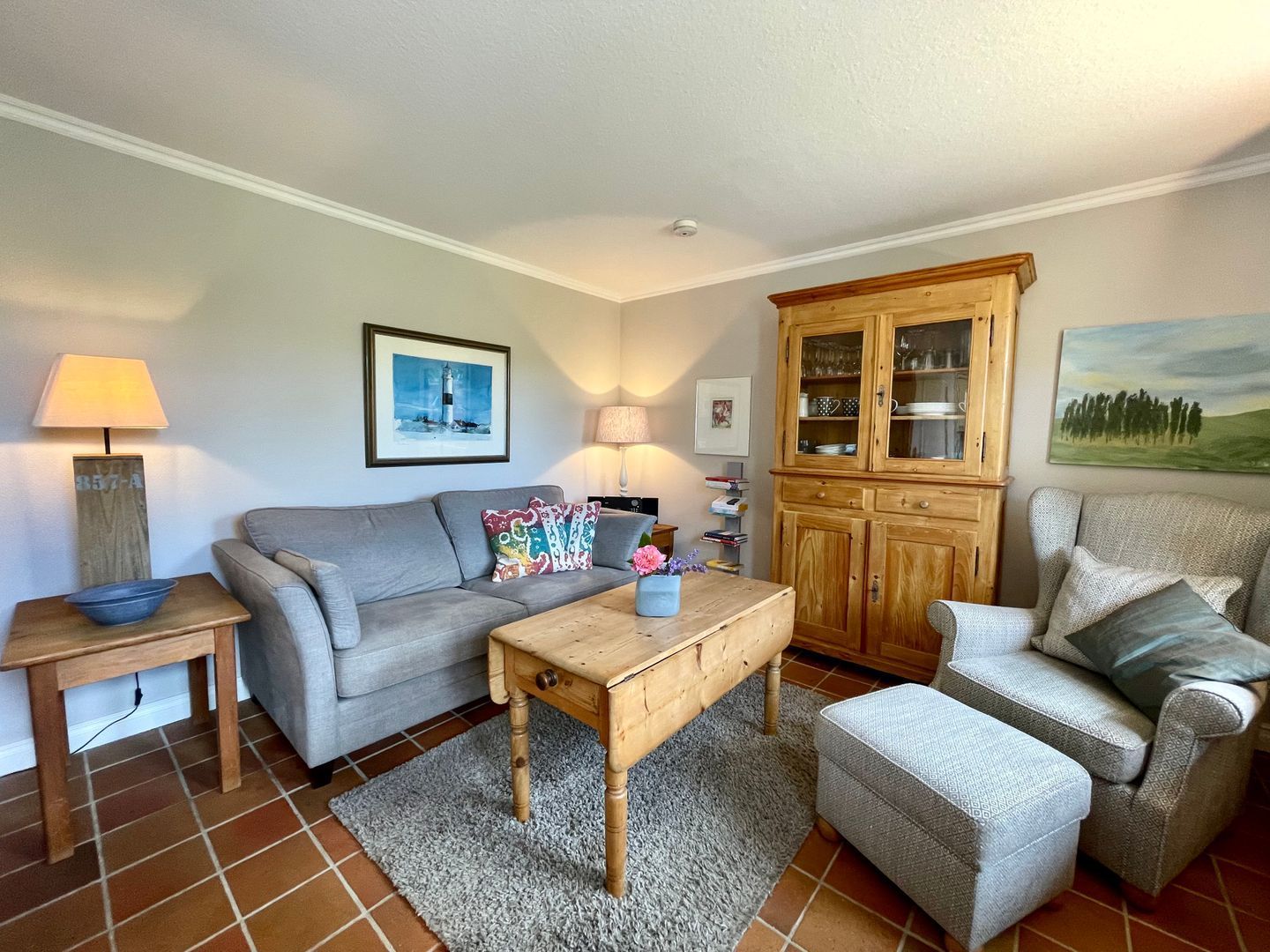A living room with a grey sofa, a wooden coffee table, a cabinet with glass doors, and a patterned rug.