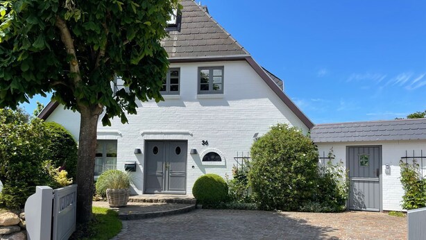 A white house with a grey door, number 36, and a small garden with a tree and bushes. - First floor, 50sqm for up to 2 persons - Haus Thomsen (Sylt)