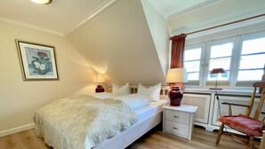A bedroom with a bed, bedside tables, a chair, and a window with curtains. - Top floor, 50sqm for up to 2 persons - Haus Thomsen (Sylt)