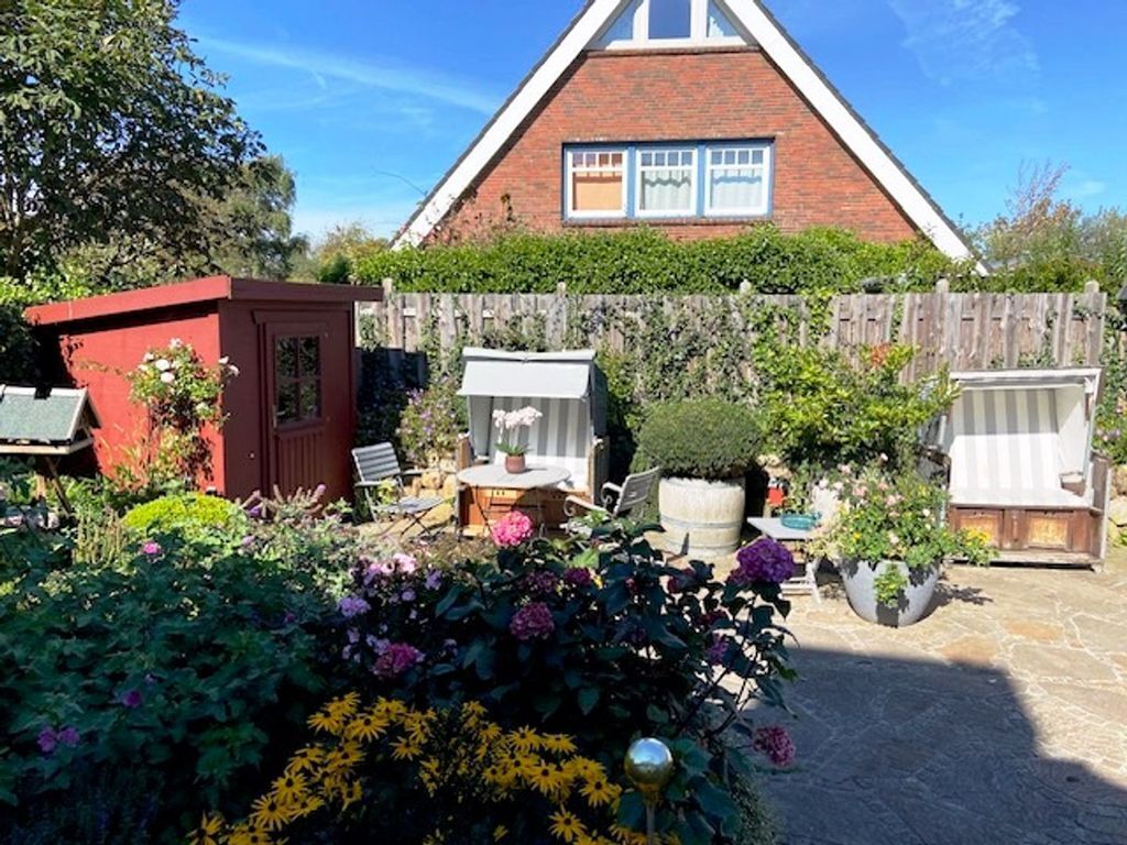 A house with a red brick exterior, a triangular roof, and a wooden fence. There is a garden with various plants and flowers, and a small red shed.