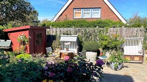 A house with a red brick exterior, a triangular roof, and a wooden fence. There is a garden with various plants and flowers, and a small red shed. - Top floor, 50sqm for up to 2 persons - Haus Thomsen (Sylt)