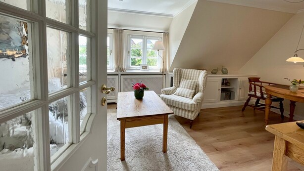 A cozy room with a wooden table, a striped armchair, and a dining table with chairs. - Top floor, 50sqm for up to 2 persons - Haus Thomsen (Sylt)