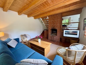 Un salon chaleureux avec un canapé bleu, des fauteuils en osier, une table basse en bois, une cheminée en briques et un téléviseur.