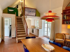 Une cuisine spacieuse avec un escalier en bois, un coin repas doté d’une grande table et un espace salon confortable.