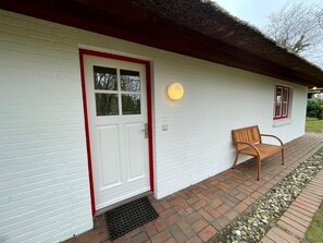 Ein weißes Gebäude mit rotem Türrahmen, einer Bank und einem kleinen Garten.