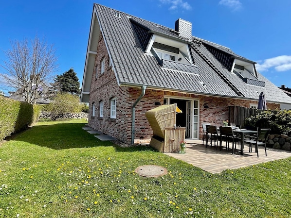 A two-story house with a sloped roof, brick exterior, and a small patio with outdoor furniture.