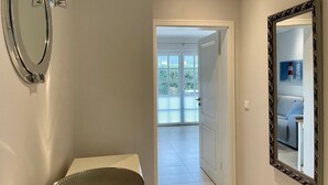 Casa de banho com sanita, lavatório e espelho. Uma porta dá acesso a uma varanda com vista para vegetação.