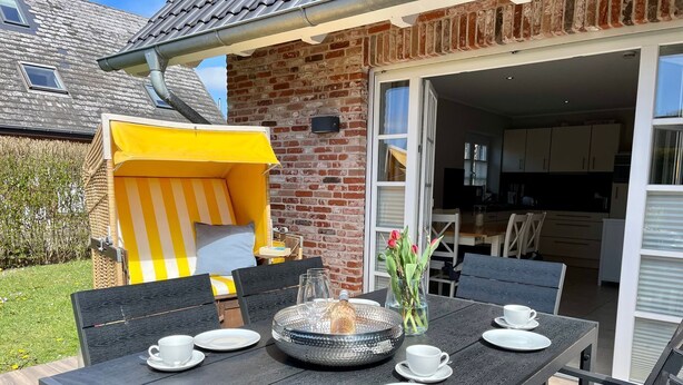 Pátio com mesa posta para dois, um guarda-sol listrado de amarelo e uma parede de tijolos.