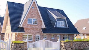 A two-story house with a stone facade, a steeply pitched roof, and a white picket fence.