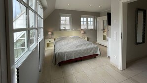 Quarto com uma janela grande, cama, guarda-roupa e espelho.