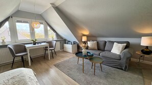 Moderni, avoimen pohjaratkaisun makuuhuone, jossa on kalteva katto, työpöytä, sohva ja sänky.