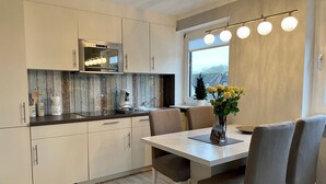 Een moderne keuken met witte kastjes, een inbouwoven en een eethoek met een tafel en stoelen.