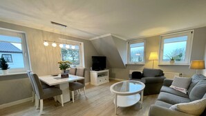Een moderne woonkamer met een eethoek, een flatscreen-tv en een bank met een kussen.