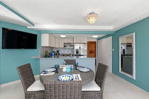 A dining area with a round table, wicker chairs, and a TV mounted on the wall.