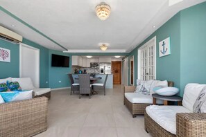 A spacious living area with wicker furniture, a dining table, and a kitchen in the background.