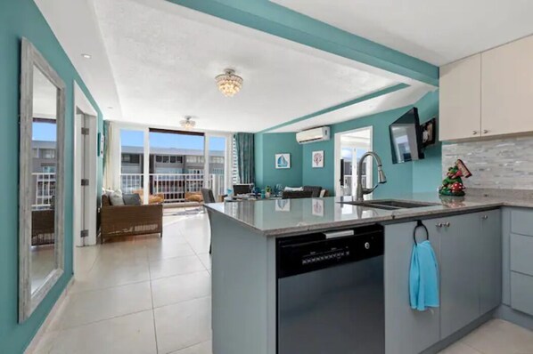 Una cocina moderna con una isla central, lavavajillas y fregadero. Hay una toalla azul colgada de la puerta del armario.