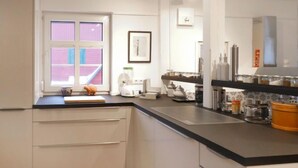 Een moderne keuken met een zwart aanrecht, witte kasten en een raam met uitzicht op een roze gebouw.