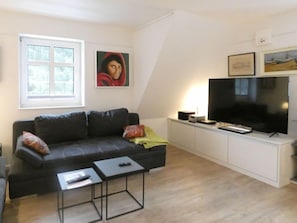 Un salon moderne avec un canapé noir, une petite table basse, un téléviseur et un tableau accroché au mur.