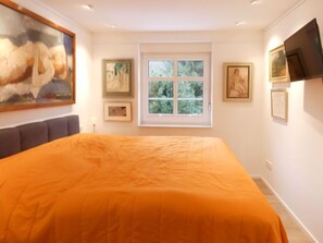 Une chambre avec un grand lit, une fenêtre et des œuvres d’art accrochées aux murs.