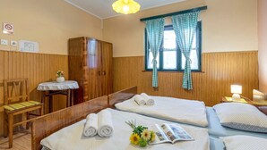 Une chambre d’hôtel avec deux lits, une armoire en bois, une petite table avec une lampe et une fenêtre avec des rideaux à carreaux.