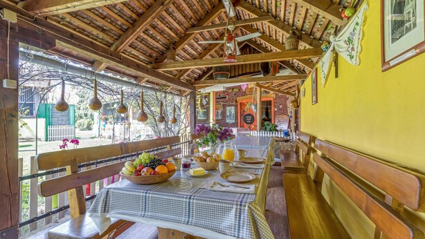 Un coin repas en bois, avec une table dressée pour le petit-déjeuner, des bancs et une vue sur l’extérieur.