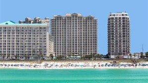 A beachfront hotel with multiple high-rise buildings, a sandy beach with umbrellas, and clear blue water. - Ariel Dunes I 303 * Last minute savings. Walk to Beach! Salt Water Vacations (Destin)